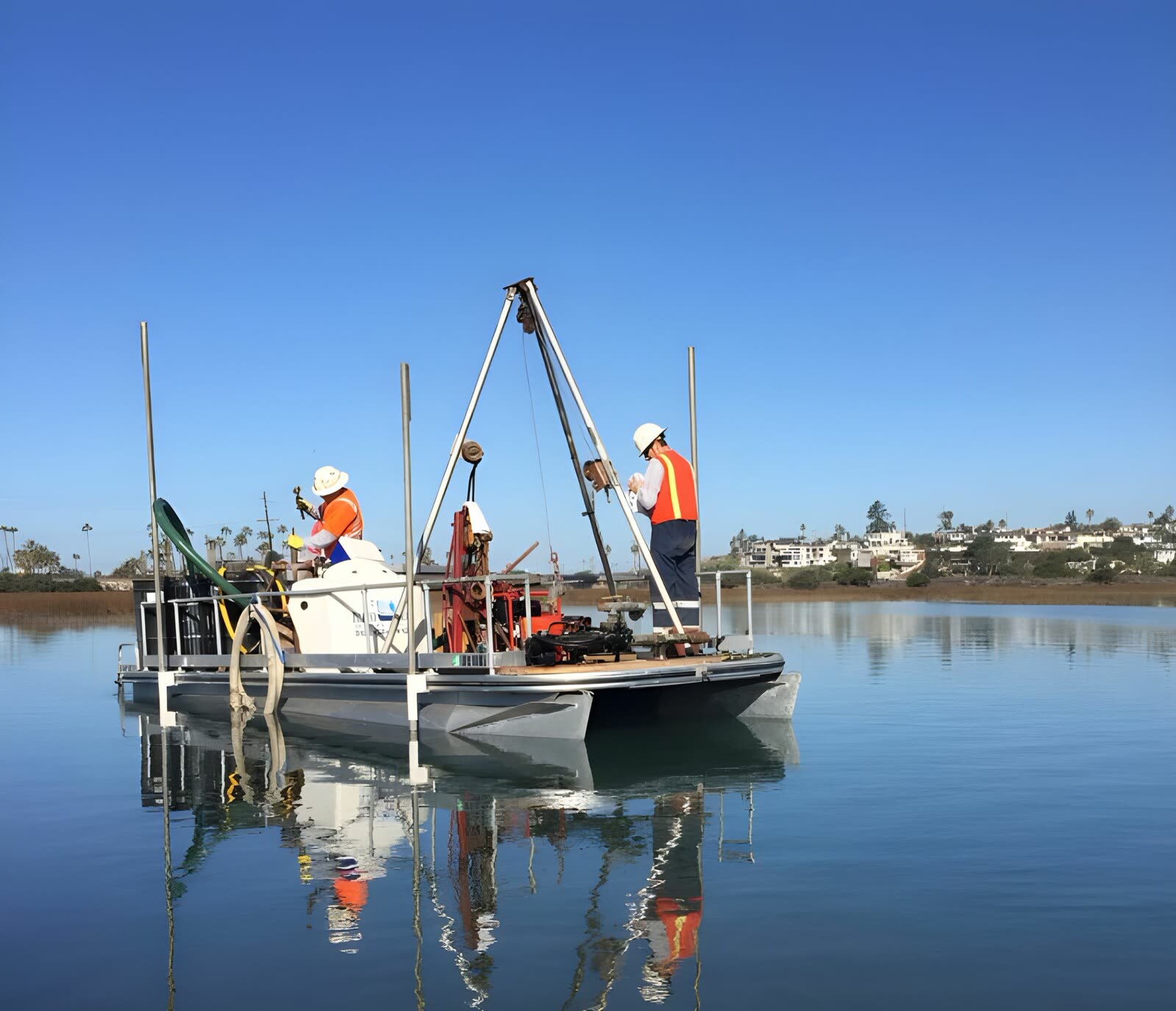 Two crew members running a tripod rig from a floating platform on a calm coastal lagoon